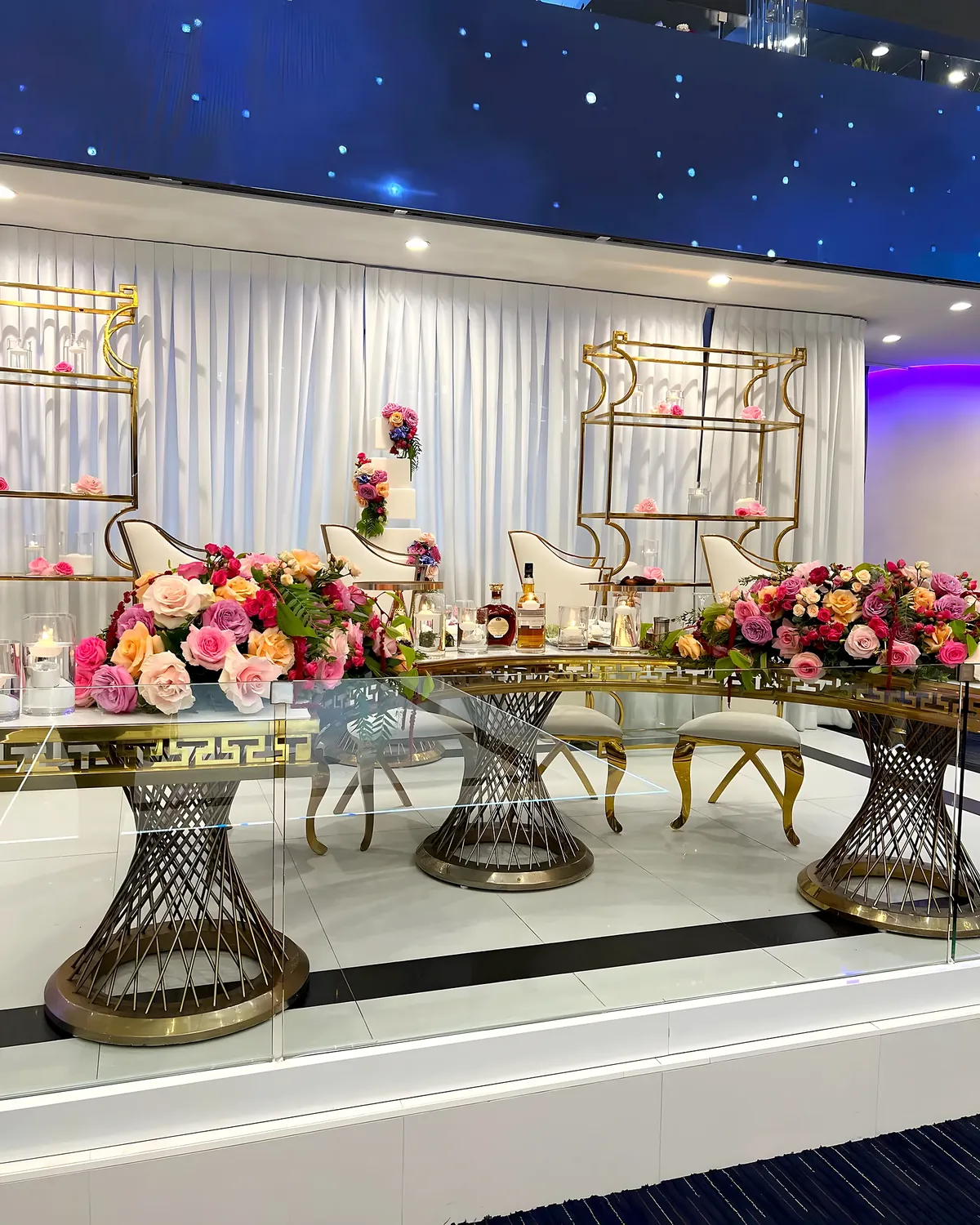 Sweetheart table with colorful roses and a tiered cake in a starlit ballroom