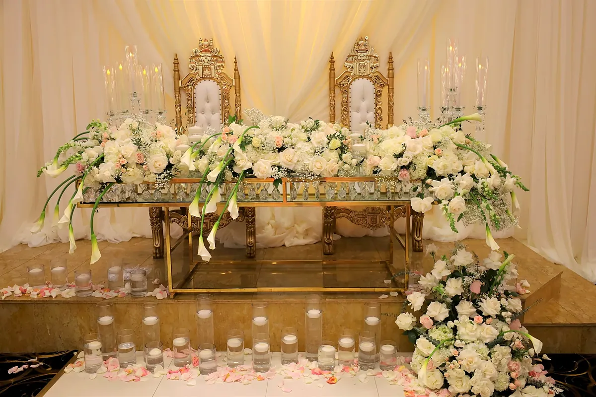 Gold thrones behind a head table covered in white roses and calla lilies